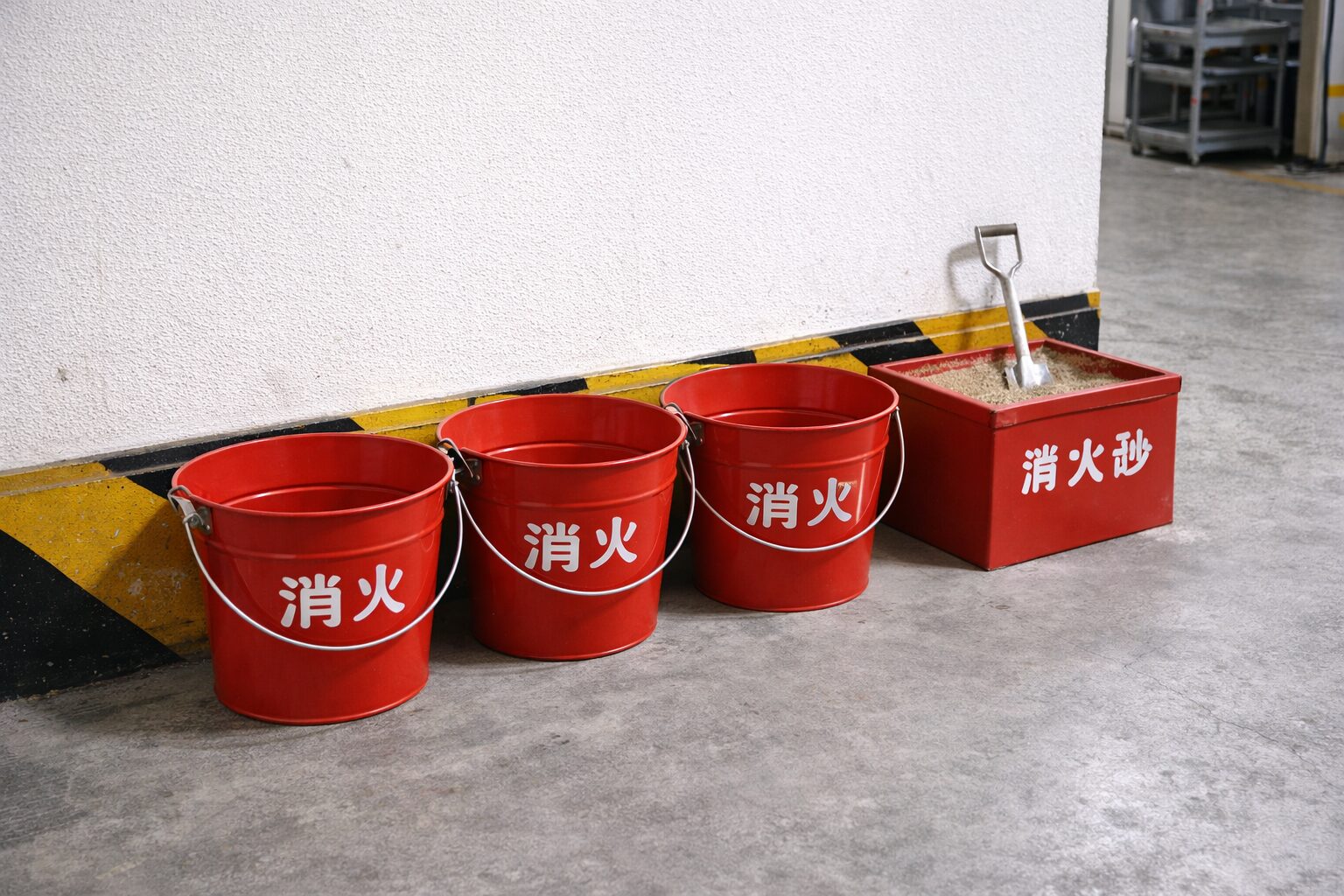赤い消火バケツ3個と消火砂箱が工場の壁際に並んでいる