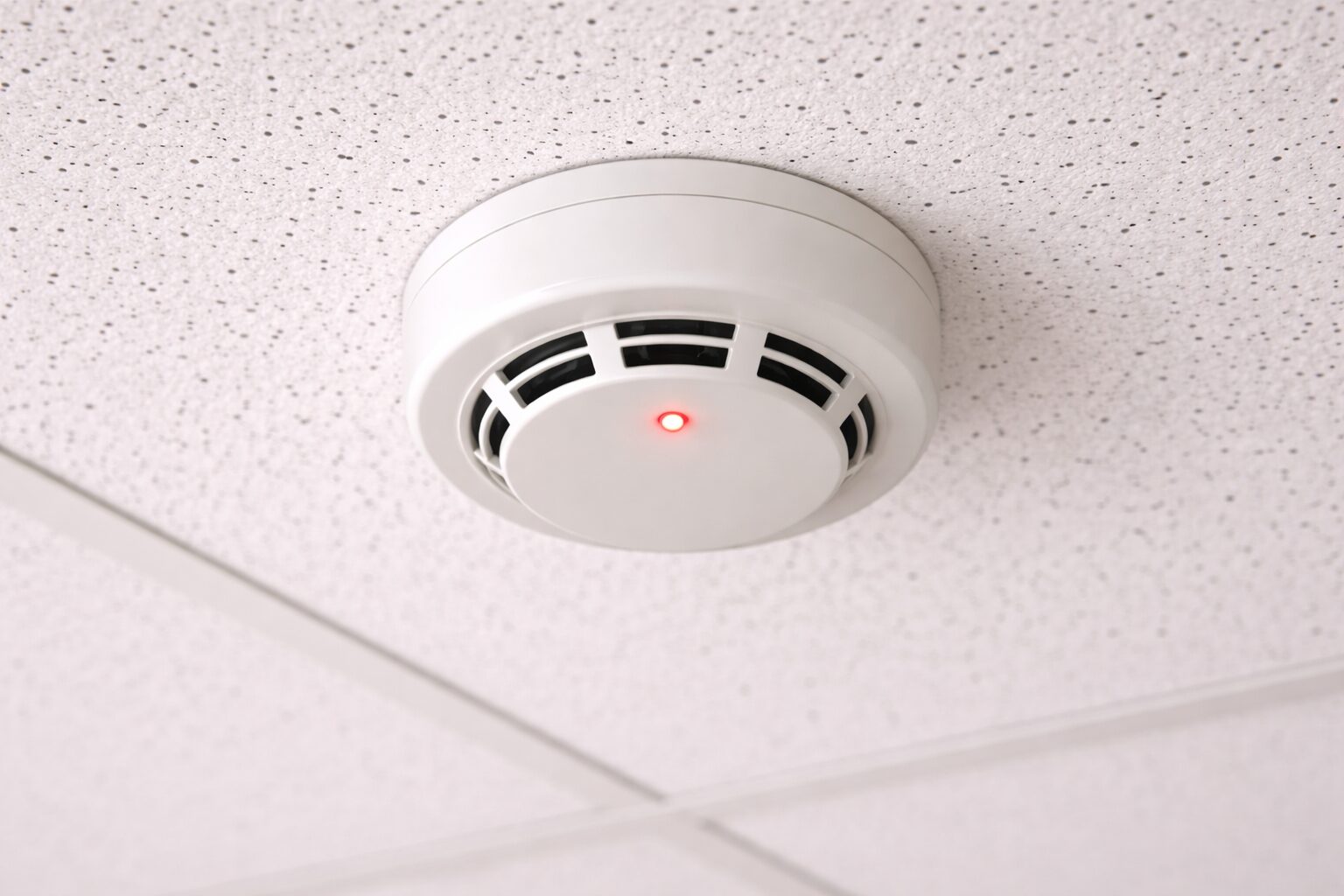 天井に設置された煙感知器。白い丸型の筐体に赤いLEDランプが光っている